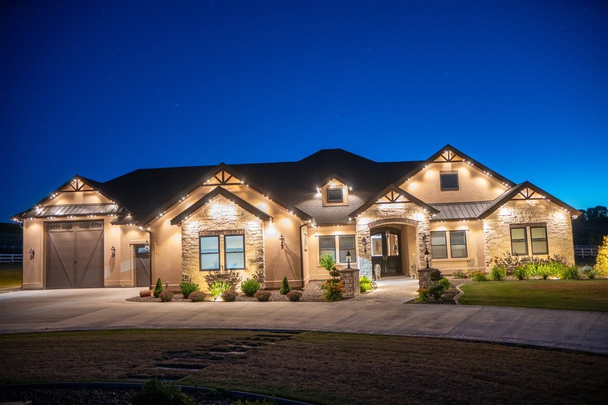 A stone and stucco home lit in warm white at dusk